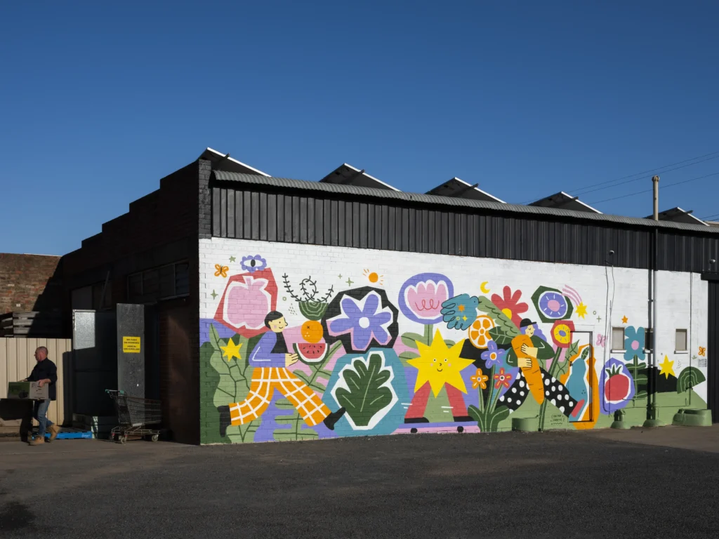 This mural is inspired by Yan Yan Candy Ng’s slow, meandering walks through the fresh produce store—where she has found so much joy in the colours, textures, and little surprises on each shelf. From fresh fruit to bunches of flowers, it celebrates the simple pleasures of daily life and the happiness found in everyday moments. This artwork was part of the 2025 Benalla Street Art Festival.